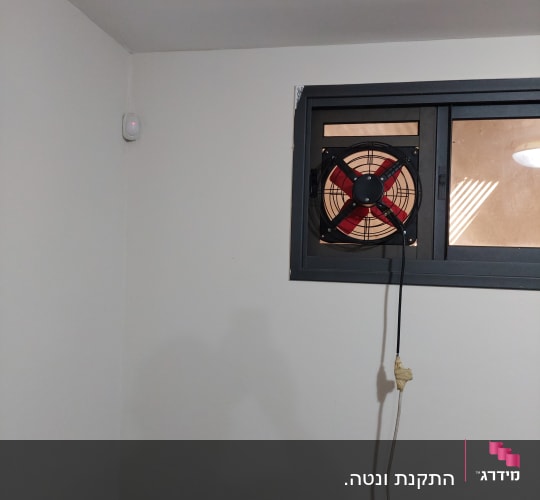 מאוורר מותקן בחלון אלומיניום עם חוט חשמל תלוי